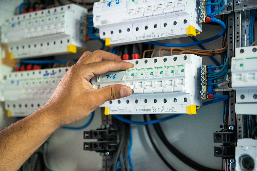 Hand eines Technikers bei der Arbeit an einem modernen Sicherungskasten mit elektrischen Schaltkreisen und Verkabelung.