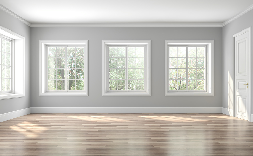 Heller, frisch renovierter Raum mit großen Fenstern, grauen Wänden und hellem Holzfußboden, ideal für modernes Wohnen.