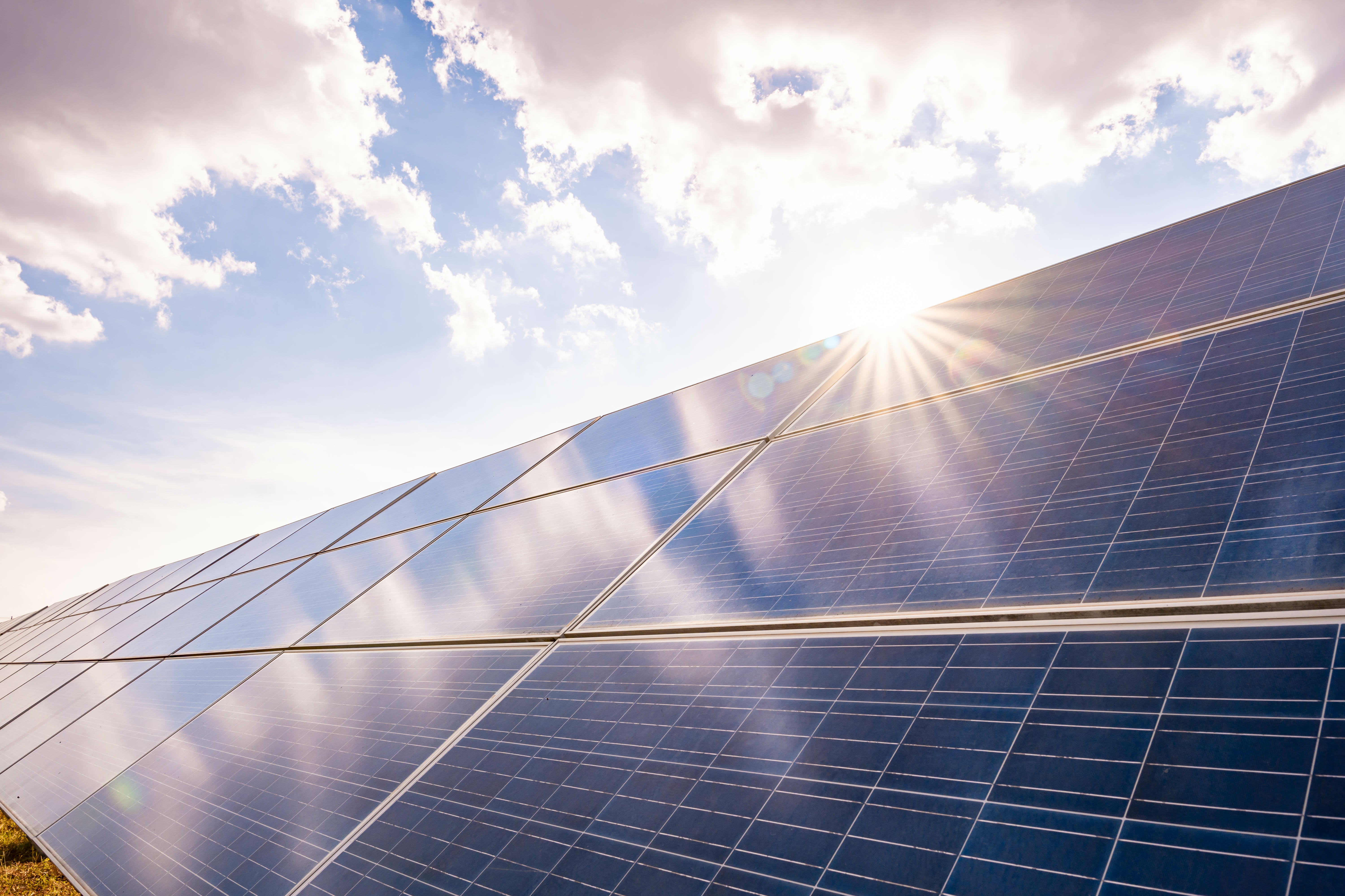 Solaranlage unter klarem Himmel mit Sonnenstrahlen, die auf die Paneele treffen, symbolisiert nachhaltige Energiegewinnung und Umweltfreundlichkeit.